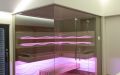 Glassauna mit Eckverglasung, Holzflächen in Wildeiche, Einrichtung in Thermo-Espe - LED Bank- und Rückenlehnenbeleuchtung, pink