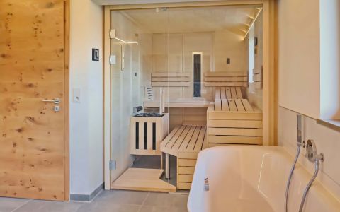 Massivholz-Sauna Fichte mit Glasfront und integriertem Gebäudefenster, Einrichtung in Linde mit verstellbarer Saunabank und Infrarotstrahler - Frontalansicht
