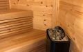 Kleine Saunakota aus Kiefernrundbohlen, außen rot und weiß gestrichen, Einrichtung in Thermoespe - Innenansicht rechte Seite, Saunabänke, Saunaofen