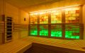 Kleine Massivholz-Sauna aus Fichte mit Glasfront, Infrarotstrahler und beleuchteter Salzsteinwand - Einrichtung und gelb-grün beleuchtete Rückwand