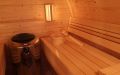 Große Fass-Sauna aus skandinavischer Fichte mit Vorraum und halbrundem Panoramafenster, Einrichtung in Espe - Innenansicht, rechte Saunabank, Saunaofen, Saunaleuchte und Aufgusseimer