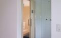 Kleine Einbausauna im Badezimmer mit Infrarotstrahler, Innen- und Außenverkleidung in Espe, Einrichtung in Linde - seitliche Ansicht mit Dusche