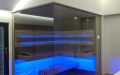 Glassauna mit Eckverglasung, Holzflächen in Wildeiche, Einrichtung in Thermo-Espe - LED Bank- und Rückenlehnenbeleuchtung, blau