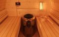 Große Fass-Sauna aus skandinavischer Fichte mit Vorraum und halbrundem Panoramafenster, Einrichtung in Espe - Innenansicht, Saunabänke, Saunaofen, Saunaleuchte und Aufgusseimer